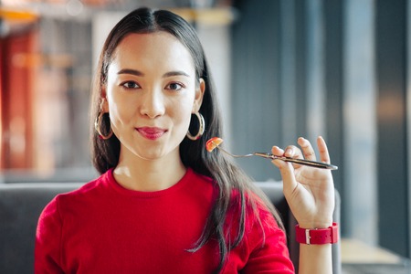 Fork with tomato. Young dark-eyed businesswoman wearing red watch holding fork with tomatoの写真素材