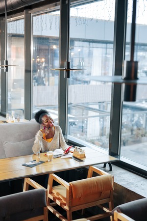 Dark-haired woman. Curly dark-haired woman sitting on grey sofa in spacious modern restaurantの写真素材