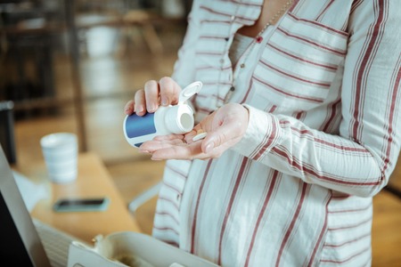Vitamin into palm. Close up of pregnant woman putting vitamin into her palm before starting workの写真素材