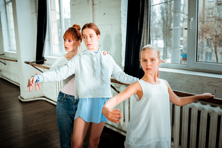 Practicing ballet positions. Blond long-haired teenager in white clothing looking focused while practicing ballet positionsの写真素材