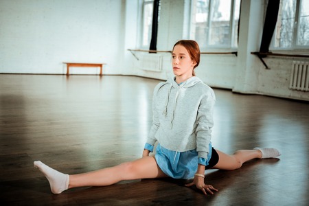 Legs-split. Pretty dark-haired teenager in black shorts looking serious while doing legs-splitの写真素材