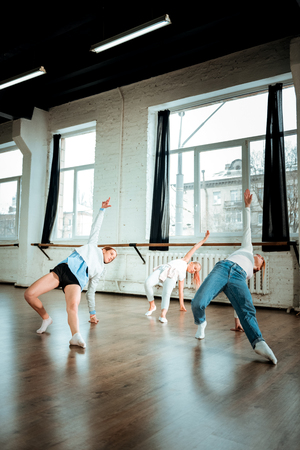 Being flexible. Red-haired dance teacher wearing blue jeans and her students doing arching while dancingの写真素材