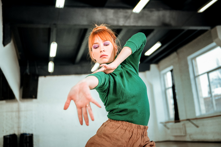 Arm - stretching. Red-haired professional choreographer wearing a green turtleneck stretching her arm while dancingの写真素材