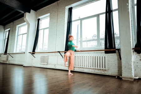 Ballet school. Young professional modern dancer with red hair looking serious while training near ballet barの写真素材