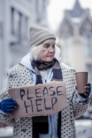 This is poverty. Unhappy cheerless woman standing on the street while looking into the cup with coinsの写真素材
