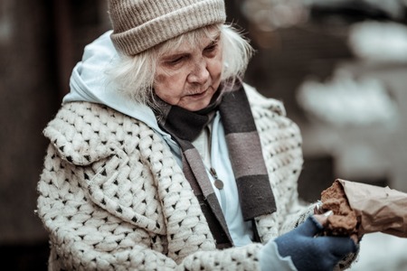Some food. Sad aged woman taking a piece of bread while eating on the streetの写真素材