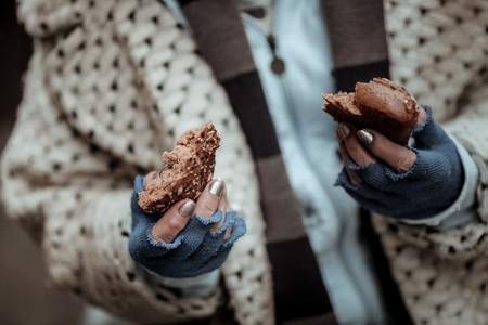 Poor life. Close up of two bread pieces being in hands of a poor homeless womanの写真素材