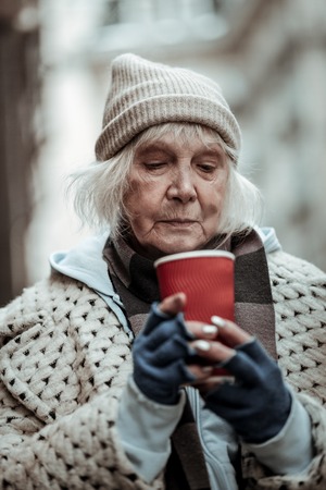 My favourite drink. Sad aged woman holding a cup with tea while looking into itの写真素材