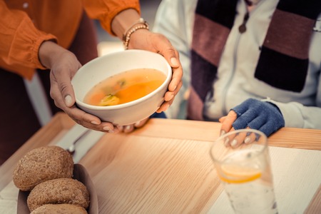 Hot meal. Bowl of tasty hot soup being in female hands while being served on the tableの写真素材