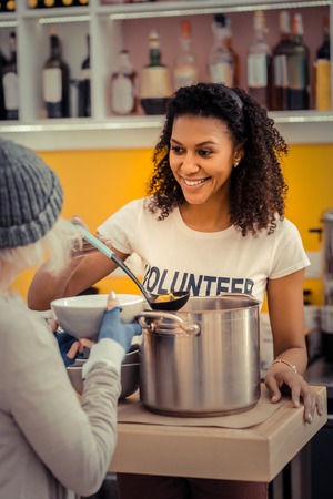 Young volunteer. Joyful nice woman giving the soup while working in the volunteer center