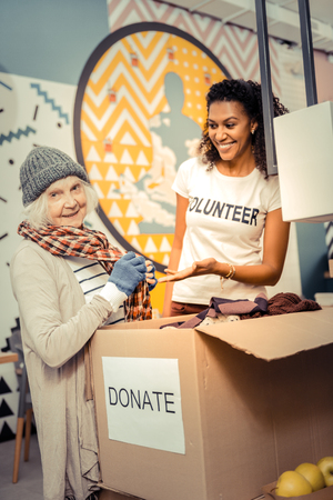 New clothes. Joyful aged woman standing near the donation box while choosing clothes for herselfの写真素材