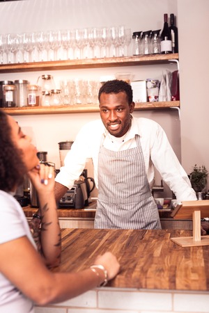 Professional barista. Cheerful positive man looking at the customer while being ready to take an orderの写真素材
