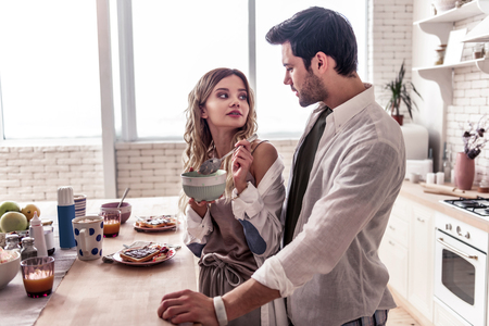 Good time. Pretty long-haired young woman wearing a white shirt and her attractive husband enjoying breakfastの写真素材