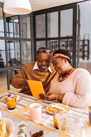 What is this. Delighted positive man pointing at the tablet screen while sitting with his wifeの写真素材