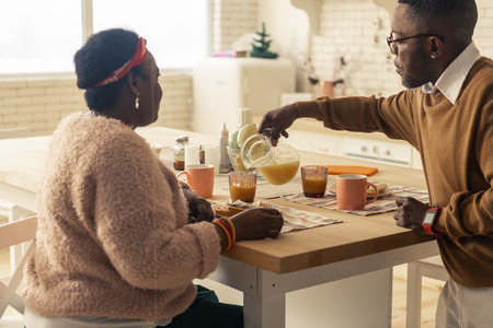 Full of vitamins. Nice handsome man pouring orange juice while caring about his wife