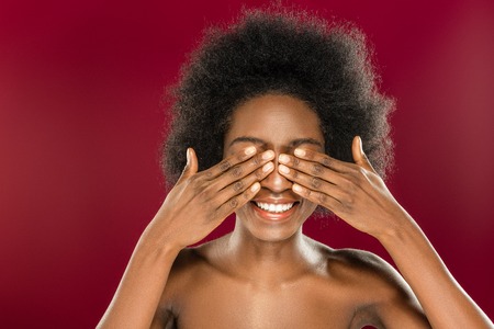Beautiful model. Cheerful positive young woman covering her eyes while standing against red...