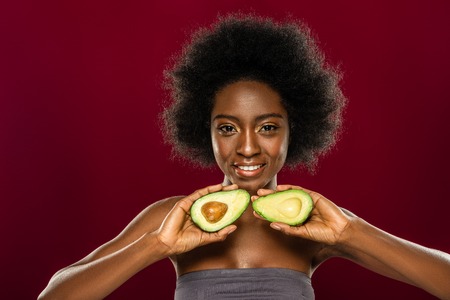 Absolutely healthy. Pleasant young woman smiling while holding avocado halves in front of her