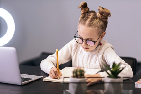 Writing. Cute blue-eyed long-haired girl wearing a white sweater writing something in a notebook