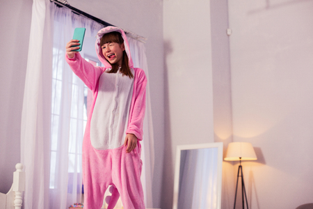 Playful mood. Cute teenager looking at screen of her gadget while keeping smile on her faceの写真素材