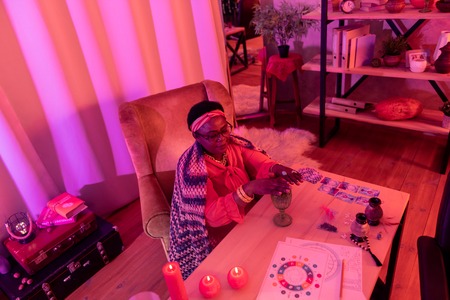 Salon. African american plump fortune-teller wearing golden watch looking busy while sitting at the...