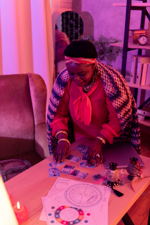 Work with Tarot. African american plump fortune-teller wearing huge earrings reading Tarot cards