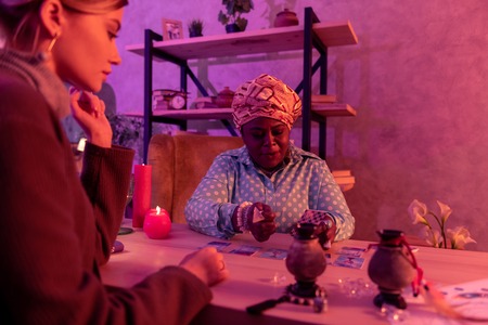 Involved into details. African american plump fortune-teller wearing a huge ring looking serious