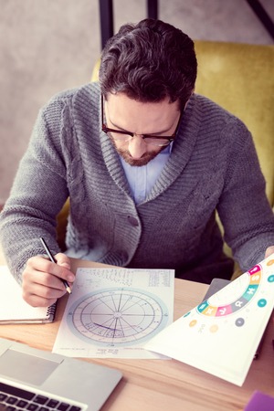 Astrological scheme. Top view of a handsome smart man looking at the drawing while making a...