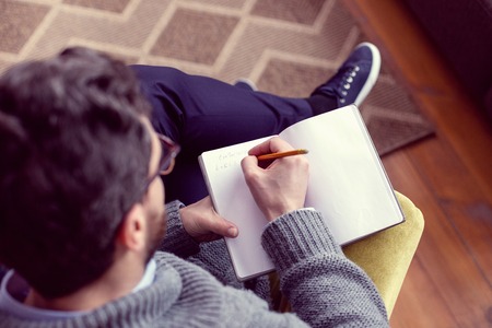 Taking notes. Top view of a serious smart man holding his notebook while writing in itの写真素材