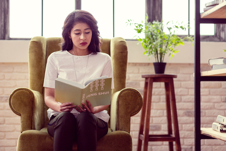 My hobby. Nice smart woman reading a book about feng shui while sitting in the armchairの写真素材