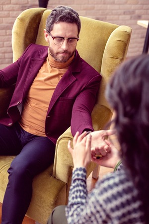 Professional chiromancer. Pleasant nice man giving his hand while being with a chiromancerの写真素材