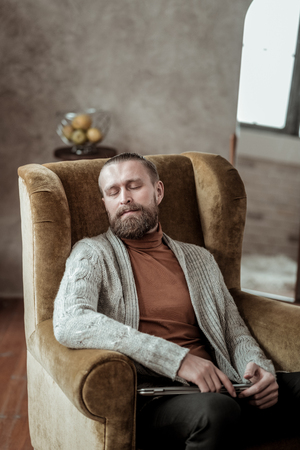Nap in armchair. Professional counselor wearing grey cardigan having nap in armchair while feeling tiredの写真素材