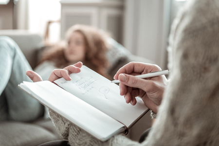 Making notes. Close up of professional psychologist making notes listening to stressed clientの写真素材