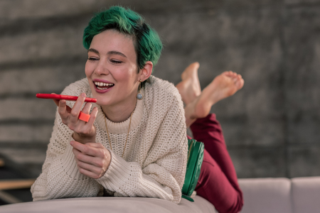 Speaking with friend. Positive woman in a good mood holding her red smartphone and speaking with friendの写真素材