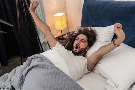 So comfortable. Nice handsome man lying in his comfortable bed while trying to wake upの写真素材