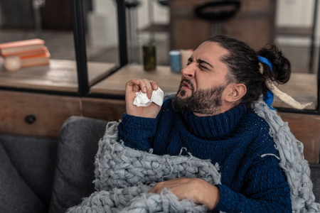 Respiratory disease. Nice ill man holding a paper tissue while sneezingの写真素材