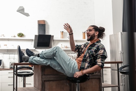 At home. Joyful delighted man sitting on the stool while relaxing at homeの写真素材