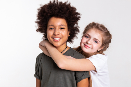 Grabbing little friend. Smiling light-haired girl hanging on her African American boy while he widely smilingの写真素材