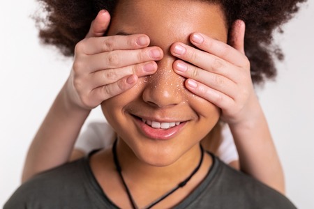 Dark-haired boy. Little girl closing eyes of her dark-skinned smiling friend with curly lush hairの写真素材