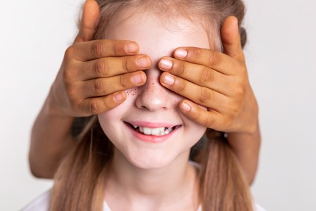 Boy closing eyes. Contented pale girl with bright freckles having closed eyes with hands of her African American friendの写真素材