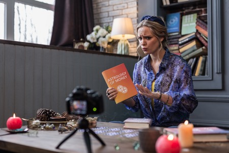 Astrology and money. Pleasant young woman speaking about an interesting book while recording a video for her blogの写真素材