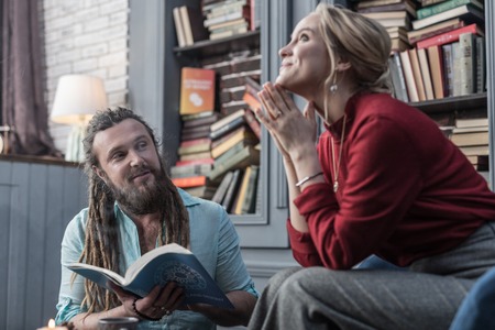 Important knowledge. Positive bearded man holding an astrological book while speaking to his client