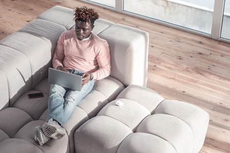 Be serious. Handsome dark-skinned man having modern hairstyle, staring at screen of his laptopの写真素材