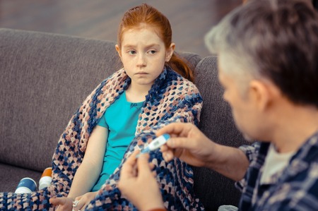 Sick child. Cheerless gloomy girl looking at her dad while worrying about her health