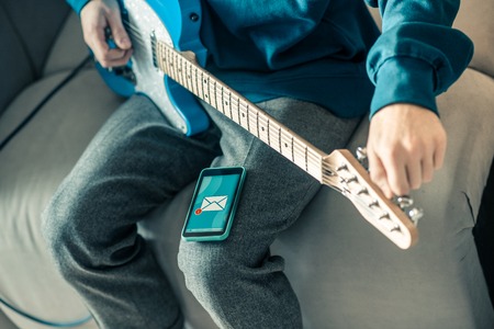 Daily repetition. Hard-working musician tuning his musical instrument and observing received message while having smartphone on lapの写真素材
