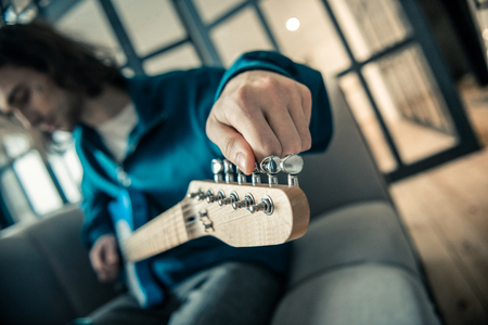 Favorite music instrument. Skilled good-looking young musician stretching strings on guitar while setting it for run-throughの写真素材