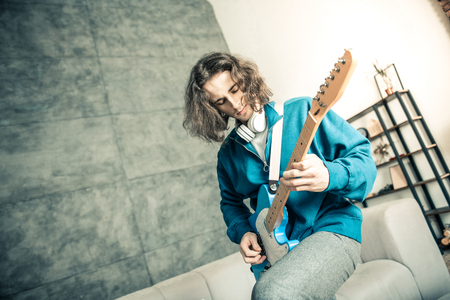 Carelessly performing. Dark-haired handsome musician having headphones on the neck while recklessly playing on music instrumentの写真素材