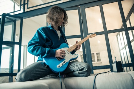 Like a rock star. Concentrated young man lying on the back of grey sofa and showing his skill in music playingの写真素材