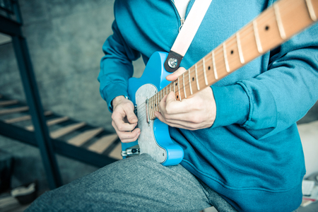 Actively playing. Professional musician in bright sweatshirt carrying blue electronic guitar while...
