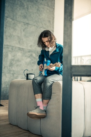 Guy with tattoo. Handsome young man being professional musician and playing at home while sitting with crossed legsの写真素材