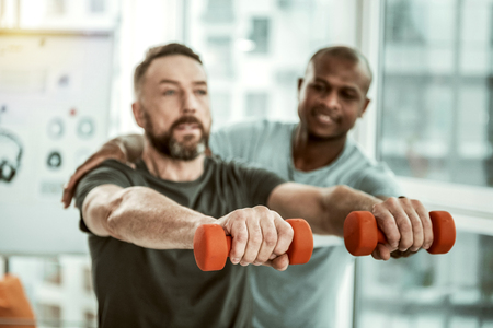Male hands. Serious bearded man looking forwards while lifting dumbbellsの写真素材